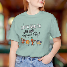Load image into Gallery viewer, Woman wearing a light green unisex t-shirt with ‘Let’s All Go to the Supper Club’ black-and-white text and cartoon characters of a brandy old fashioned, golden dinner roll, relish tray, and blueberry cheesecake.